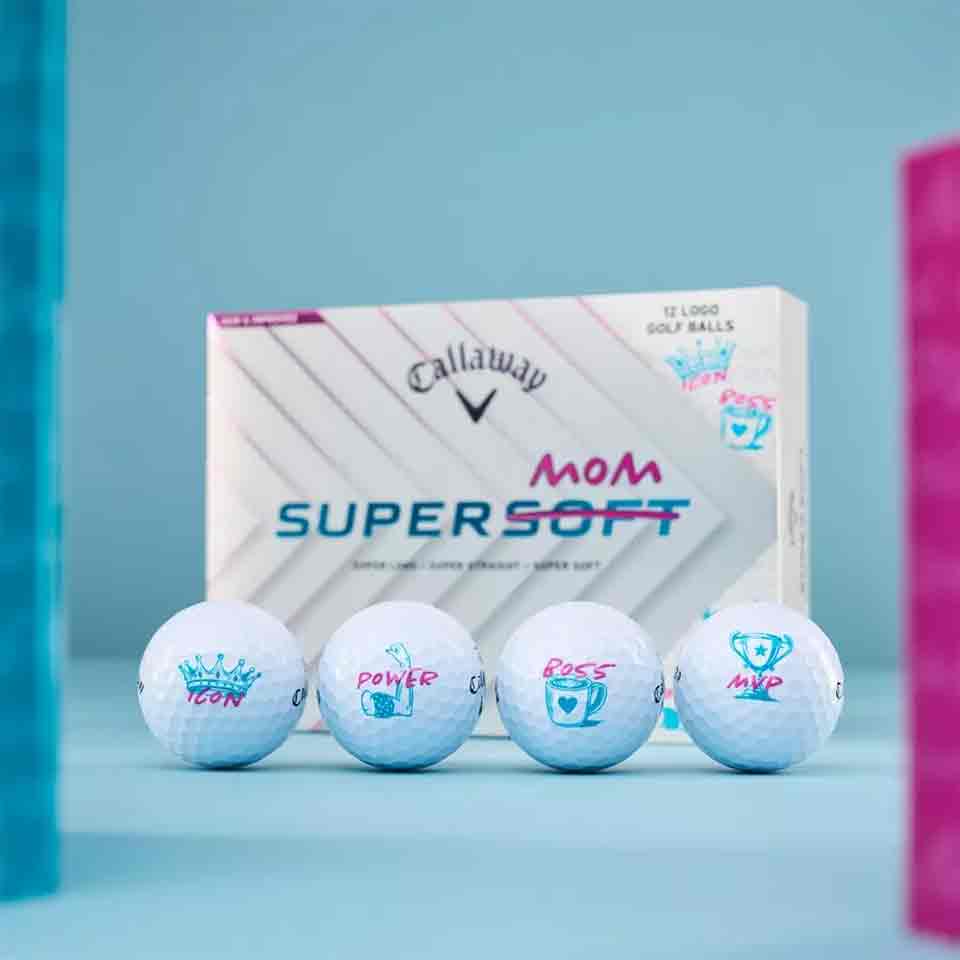 Four Callaway golf balls with hand-drawn designs and words like ICON, POWER, BOSS, and MVP are lined up in front of a Callaway Supersoft Mom box&mdash;perfect as stylish accessories or unique Mother&rsquo;s Day gifts. Pink and blue objects frame the image.