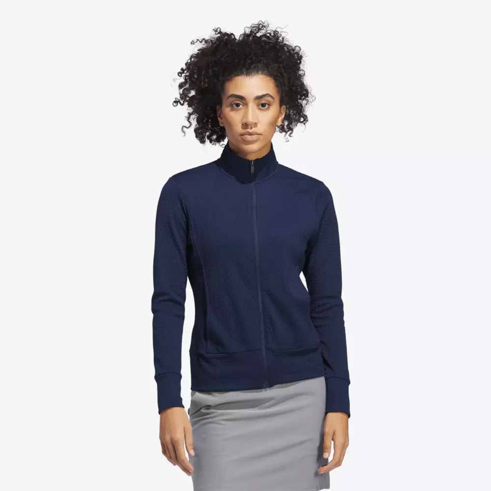 A woman with curly hair is wearing a navy blue zip-up jacket and a light gray skirt, showcasing stylish apparel perfect for Mother&rsquo;s Day, standing against a plain white background.