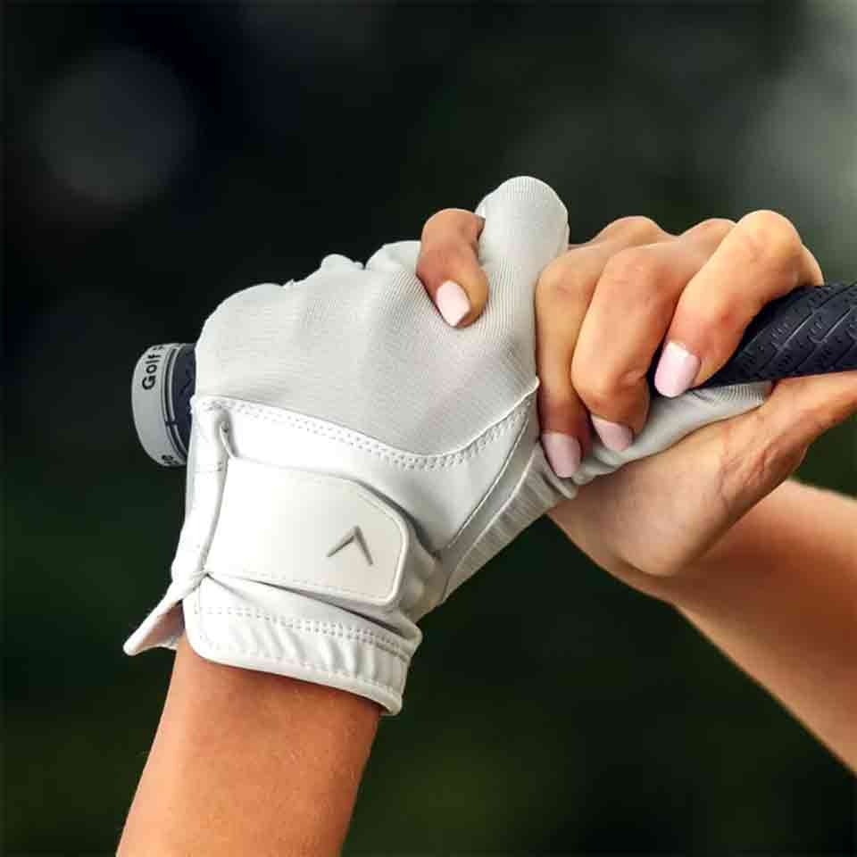A close-up of two hands gripping a golf club&mdash;one in a white glove, the other with pale pink manicured nails&mdash;captures a special Mother's Day moment. The background is softly blurred, highlighting this intimate gesture.