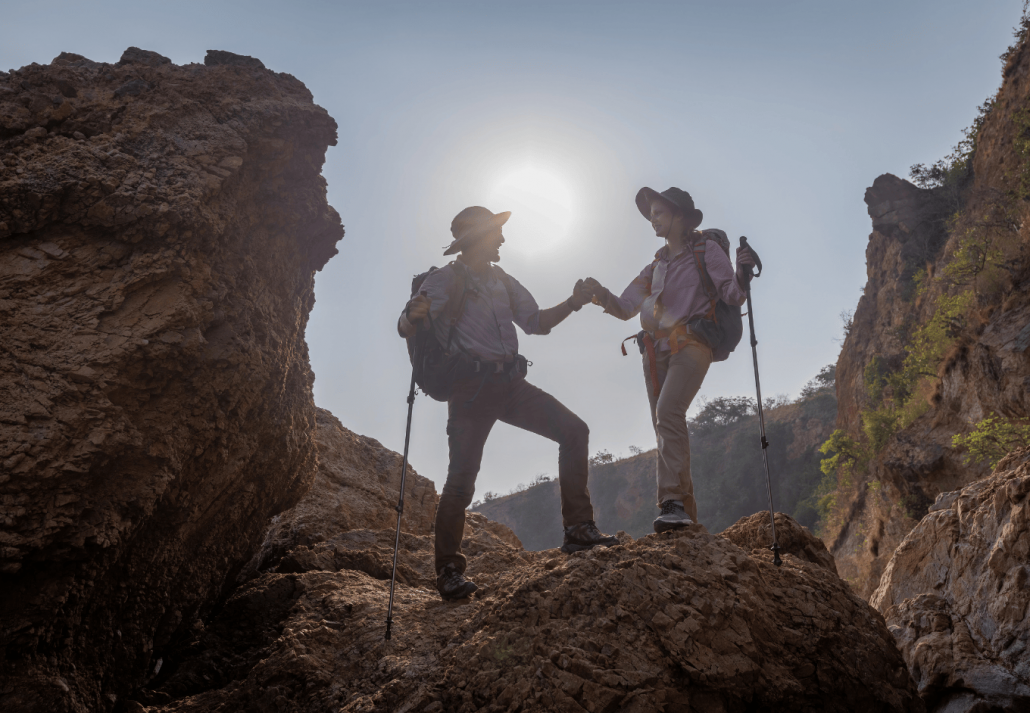 Tourists show helping young woman with backpacks hike on rocky top mountain trekking and soft foggy