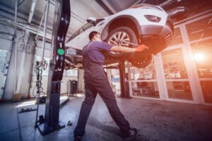 Car mechanic inspecting wheel and suspension detail of lifted automobile at repair service station