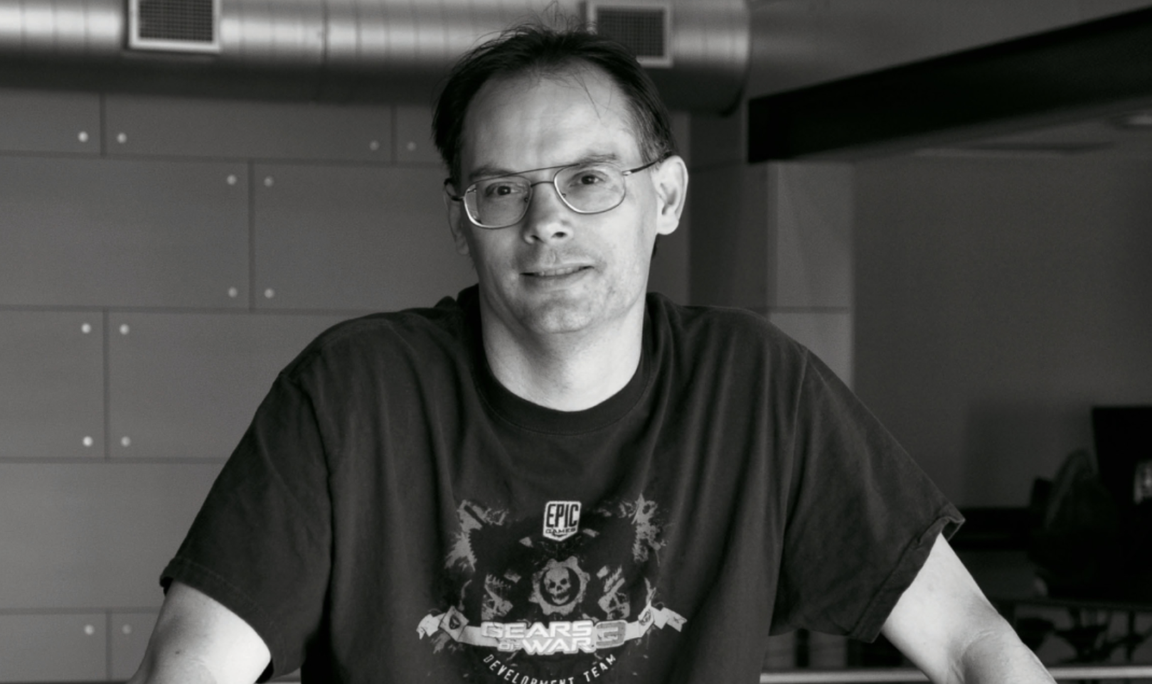 Epic co-founder Tim Sweeney smiles at the camera while wearing a Gears of War t-shirt, in a black-and-white portrait.