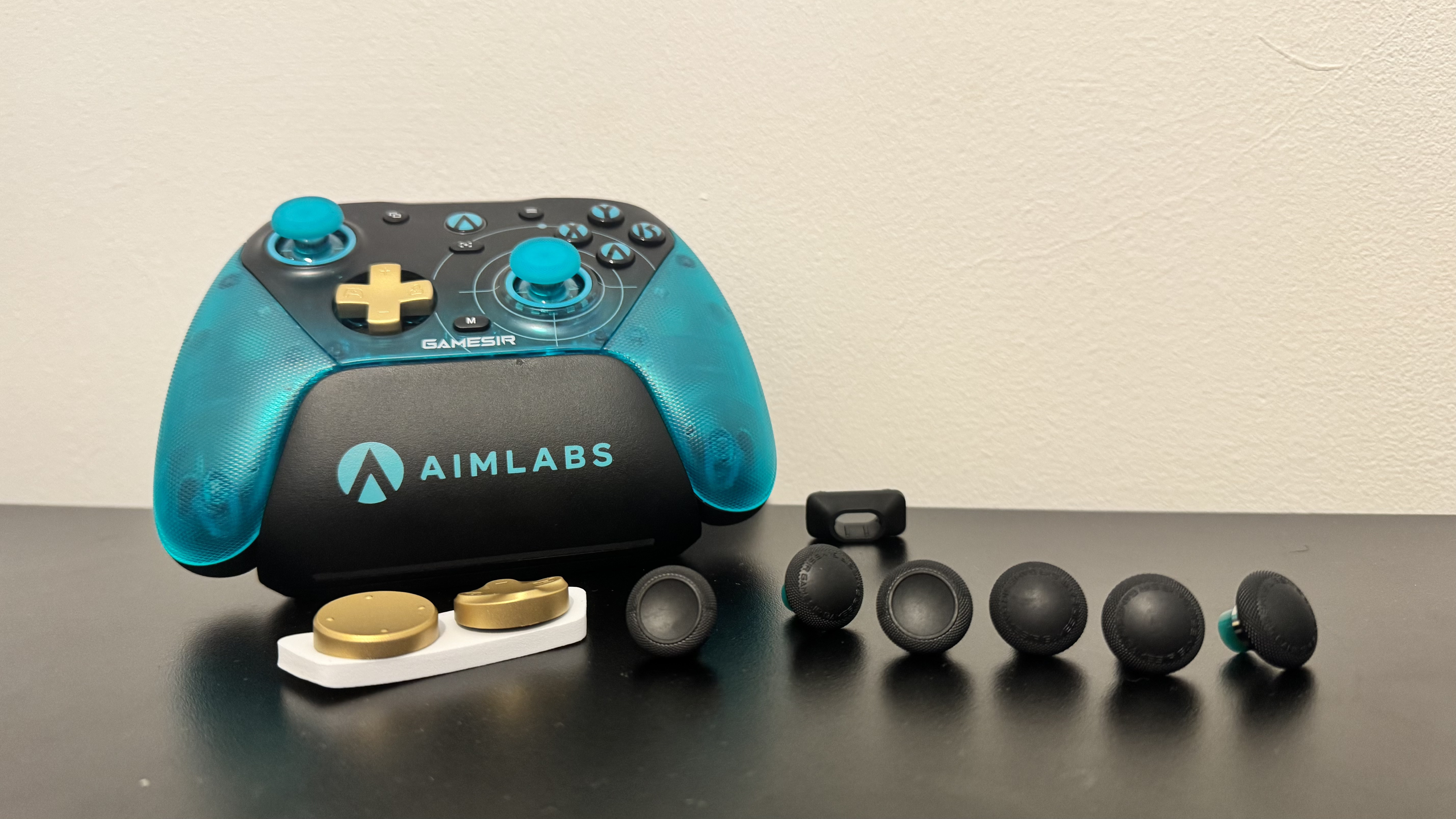 The GameSir G7 Pro 8K Aimlabs Edition on its stand on a black table, with spare D-Pads and thumbsticks nearby