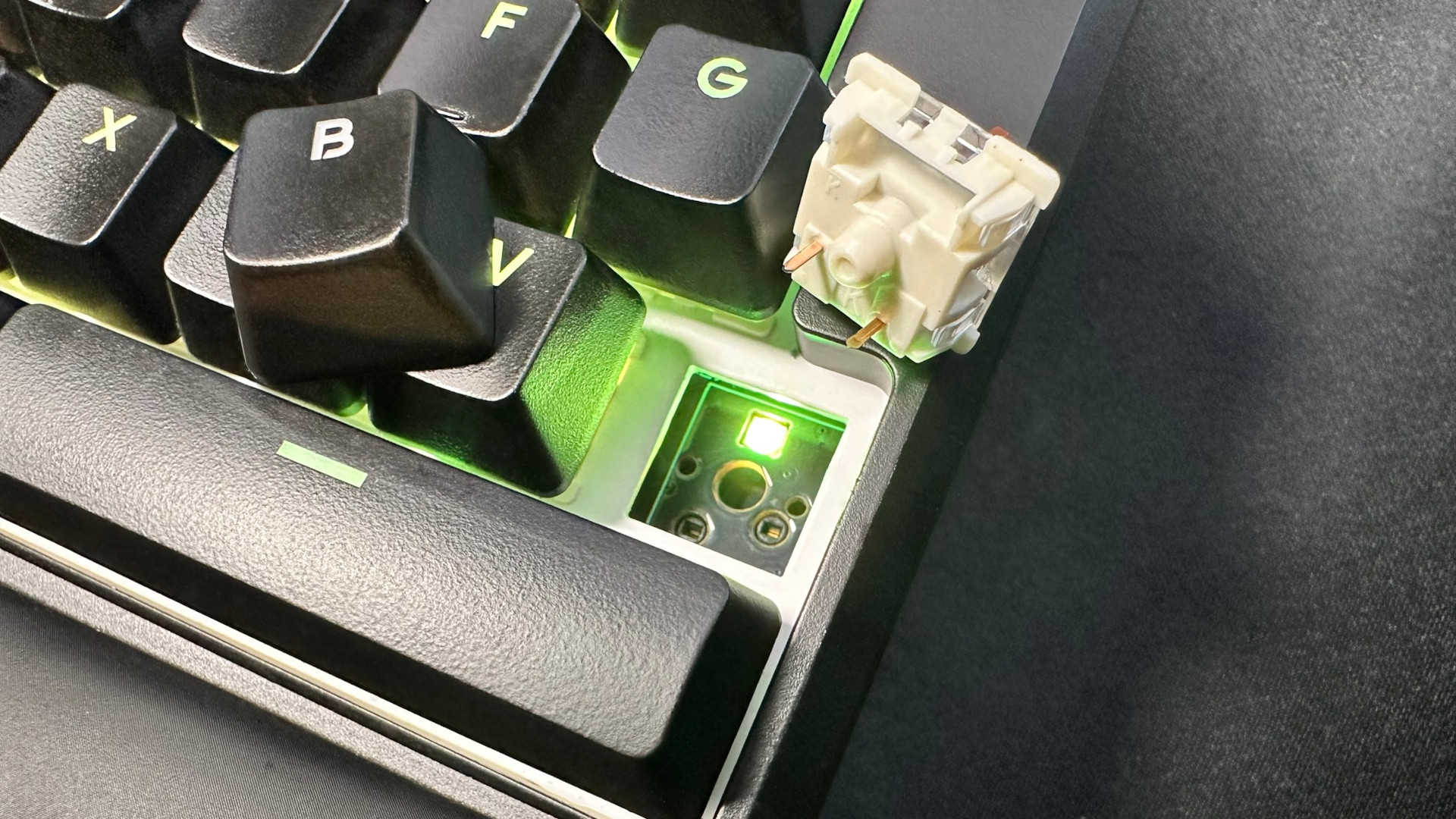 A photograph of the Kinesis Gaming Freestyle Edge RGB Plus ergonomic keyboard, showing a key and switch removed from the hot-swappable PCB