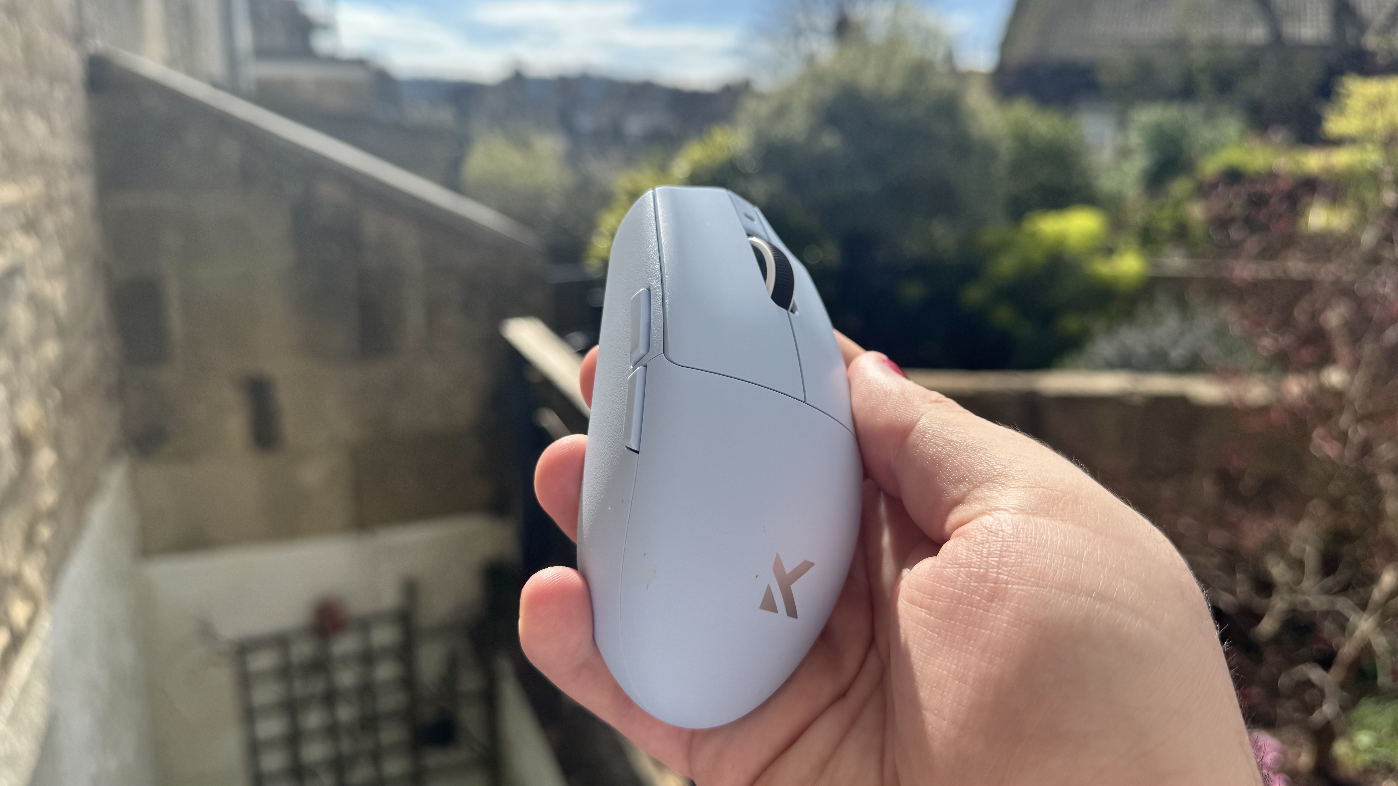 The blue Mchose G3 V2 gaming mouse from the side, in a hand in a garden