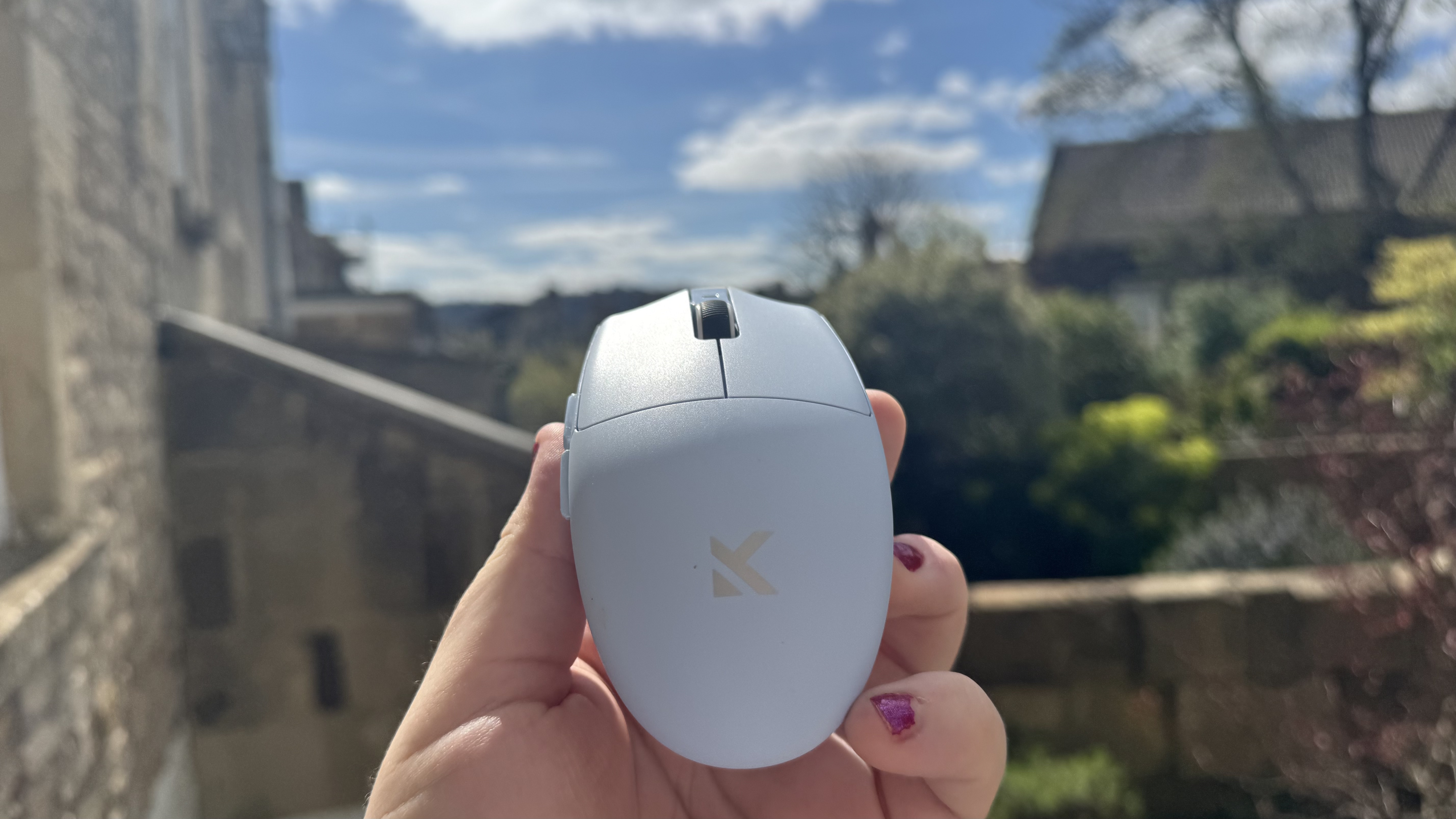The blue Mchose G3 V2 gaming mouse from the back, in a hand in a garden