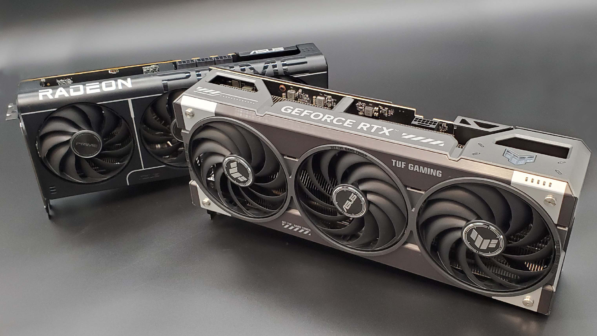 The Asus TUF Gaming RTX 5070 Ti OC Edition in front of the Asus Prime RX 9070 XT on a silver background