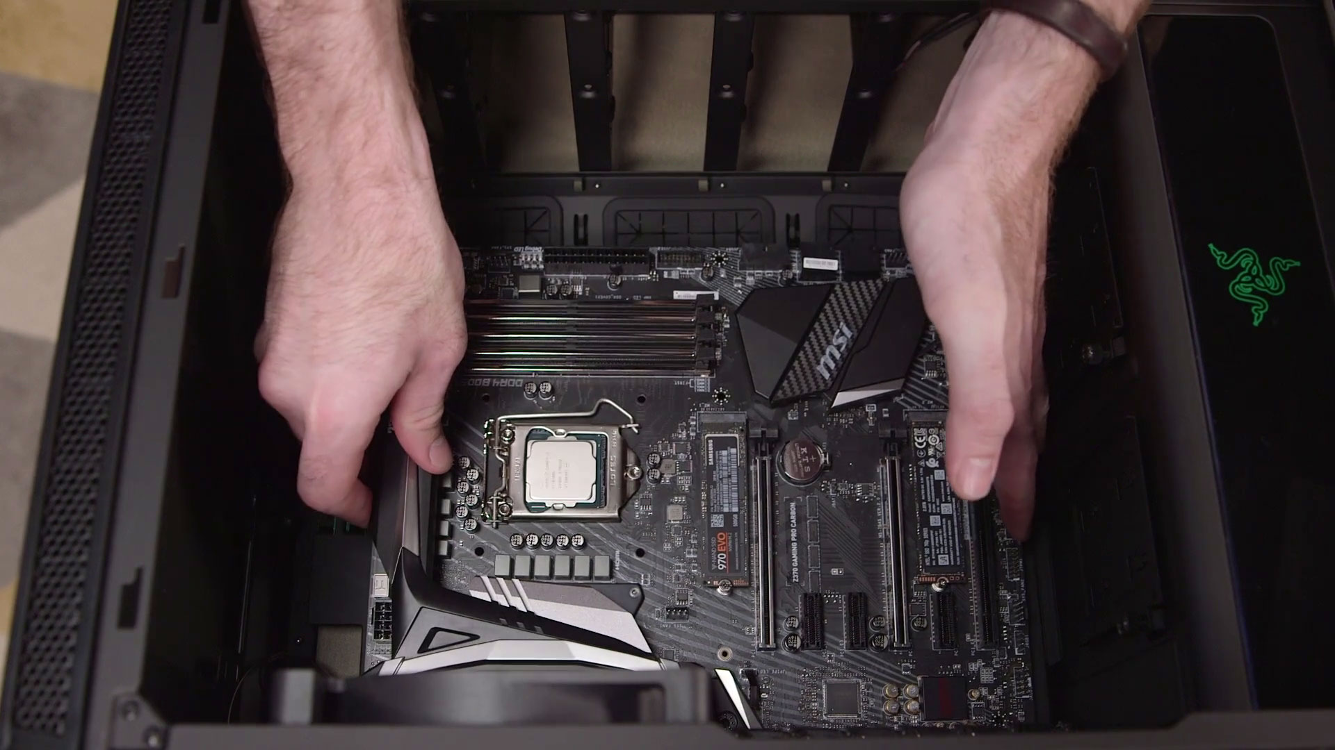 We see a pair of hands installing a motherboard inside of a PC case.