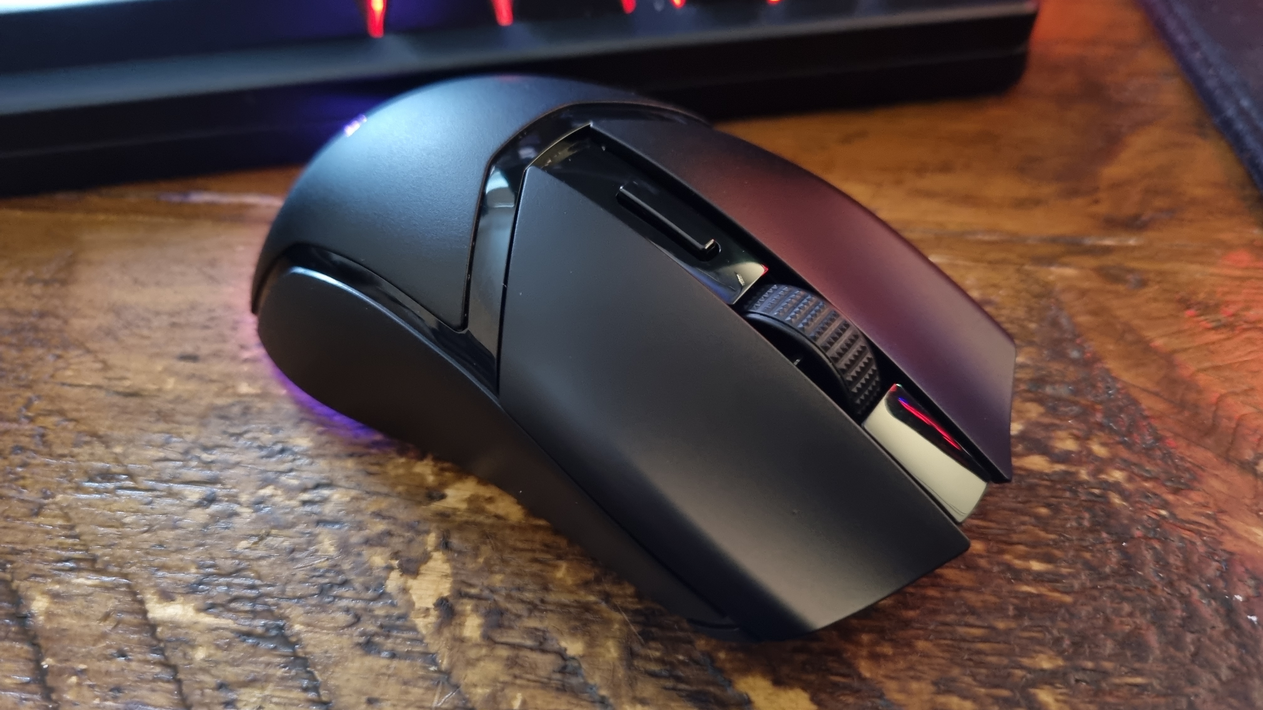 A Razer Cobra HyperSpeed gaming mouse on a wooden desk with its RGB lighting lit in various colours