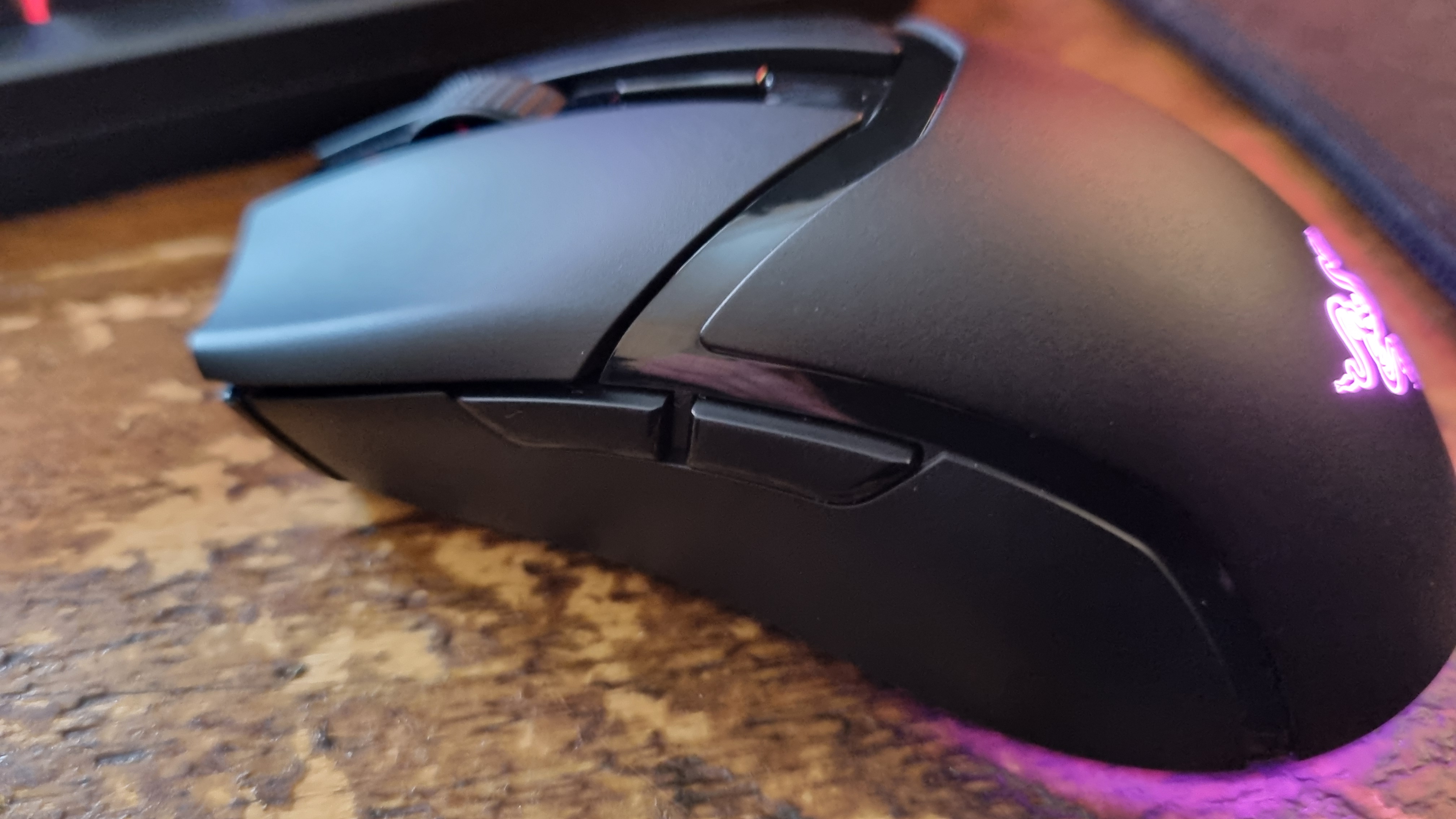 A Razer Cobra HyperSpeed gaming mouse on a wooden desk with its RGB lighting lit in various colours