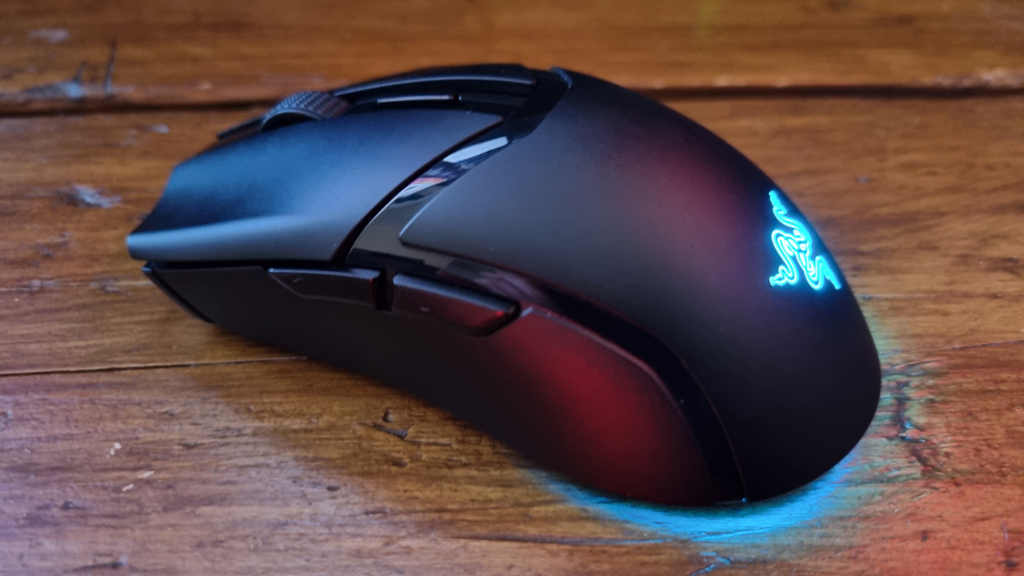 A Razer Cobra HyperSpeed gaming mouse on a wooden desk with its RGB lighting lit in various colours