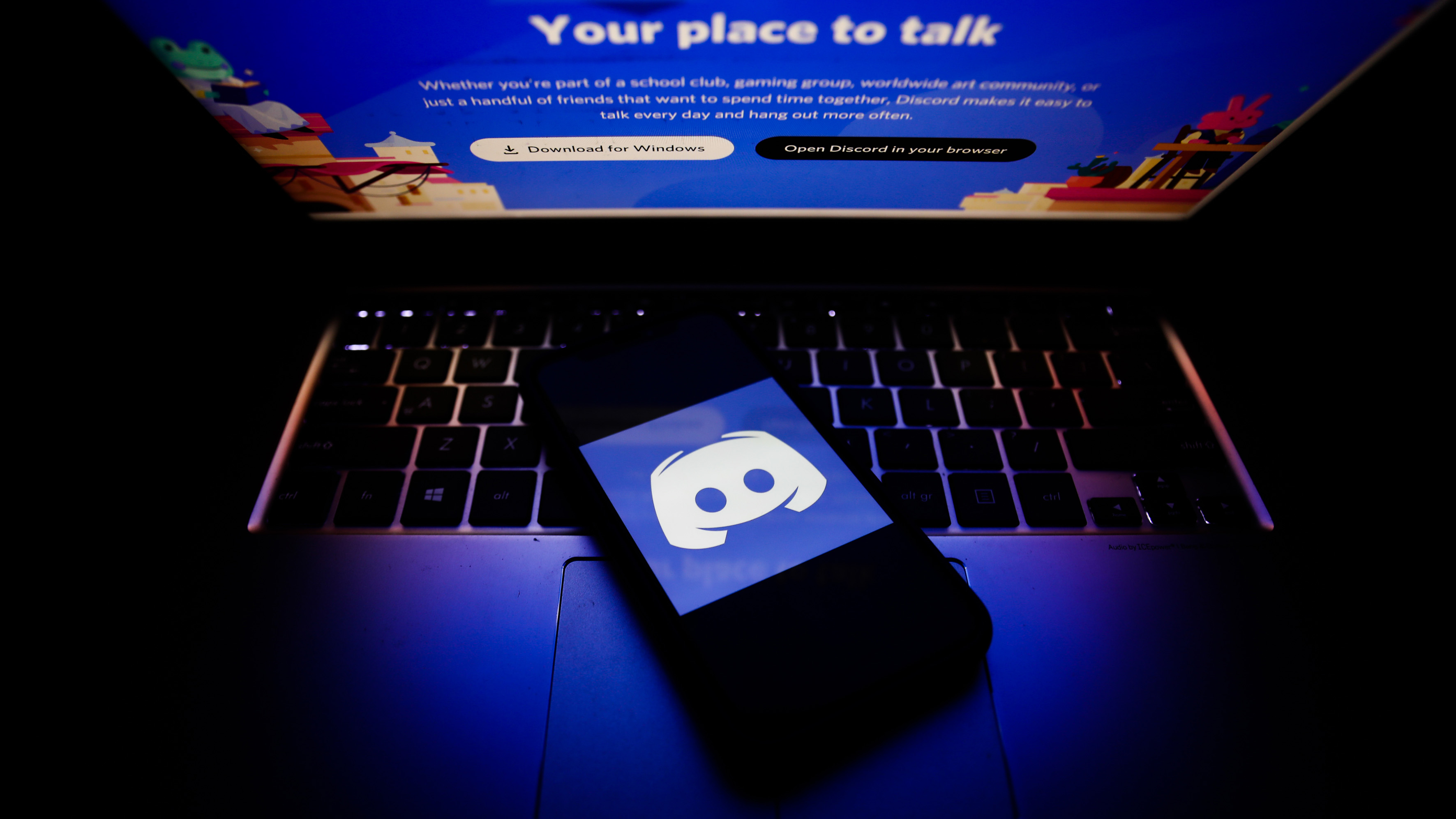 The Discord logo on a phone on top of a dark laptop