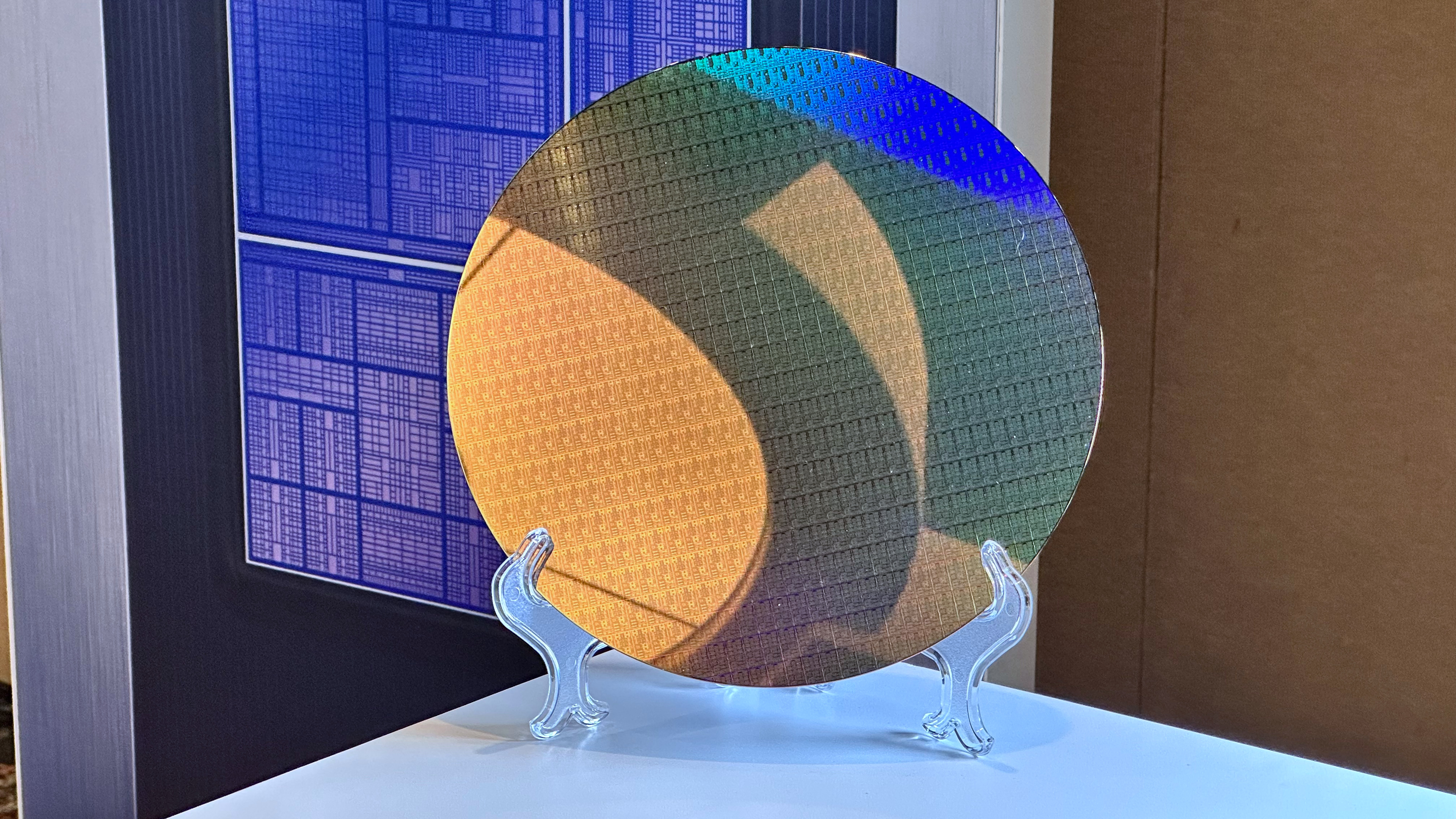 A photo of an Intel 18A wafer, full of Panther Lake compute tiles, with a stylized image of a complete PTL chip in the background.