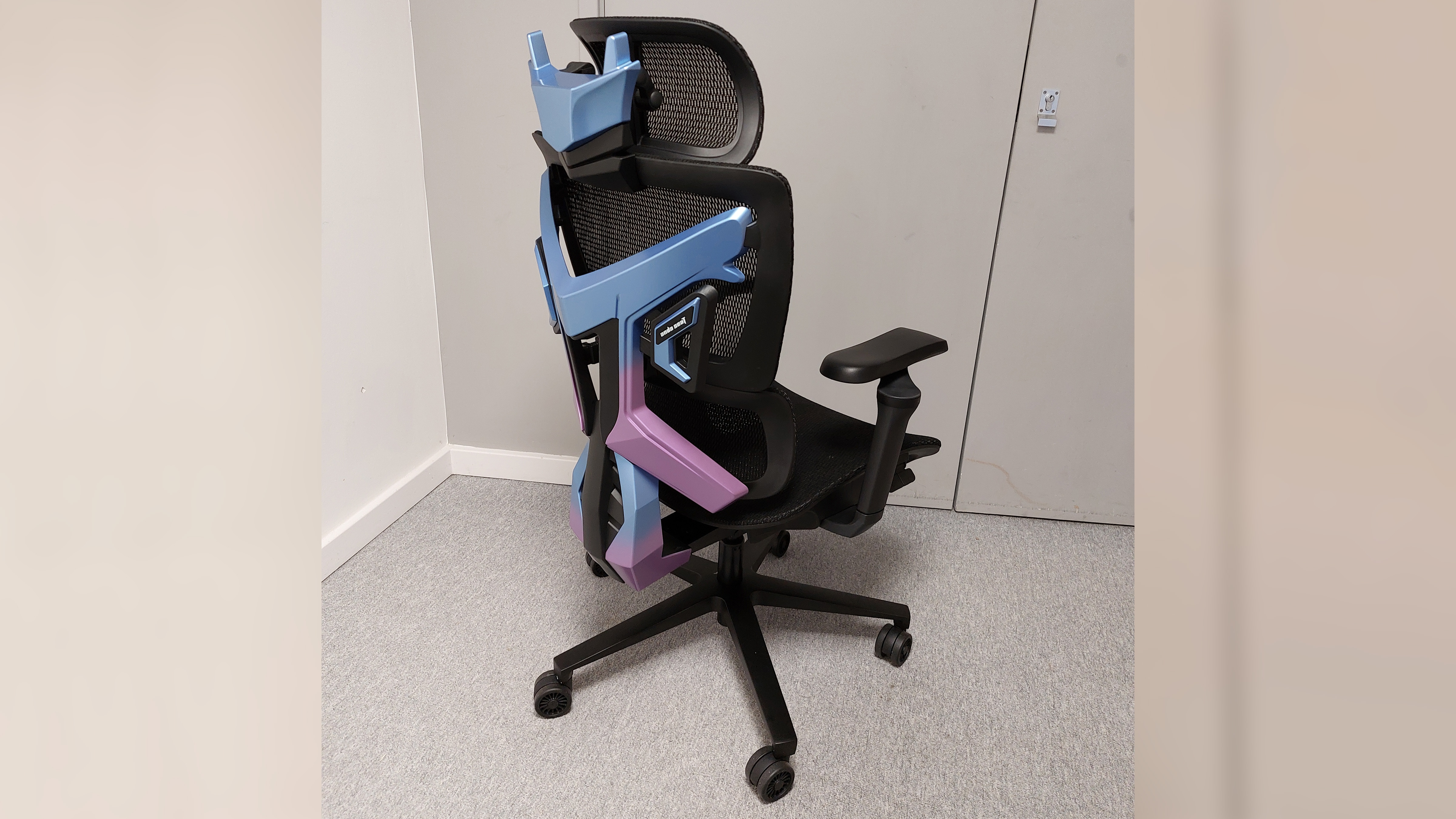 A 3/4 view of the AndaSeat X-Air Pro. The entire chair is in shot, and from this angle it is very clear that this is just a fancy office chair with a hefty hunk of colourful plastic strapped to the back of it for a bit of 'gamer flair'.