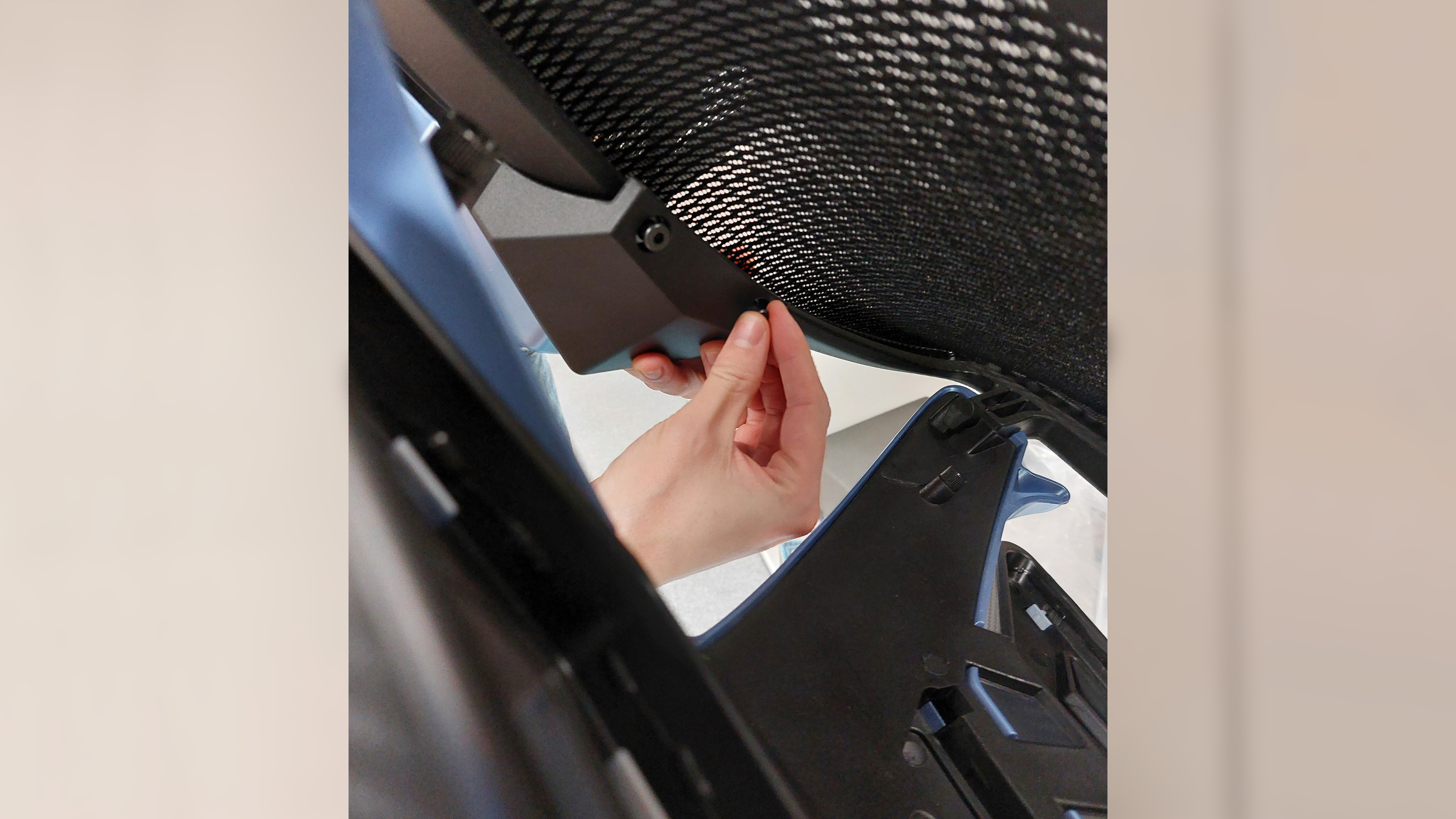 A different hand attempts to directly adjust the tightness of screws attached to the AndaSeat X-Air Pro back rest, beneath and seperate to the hefty plastic back frame which is partially obscuring the lower left corner of the frame.