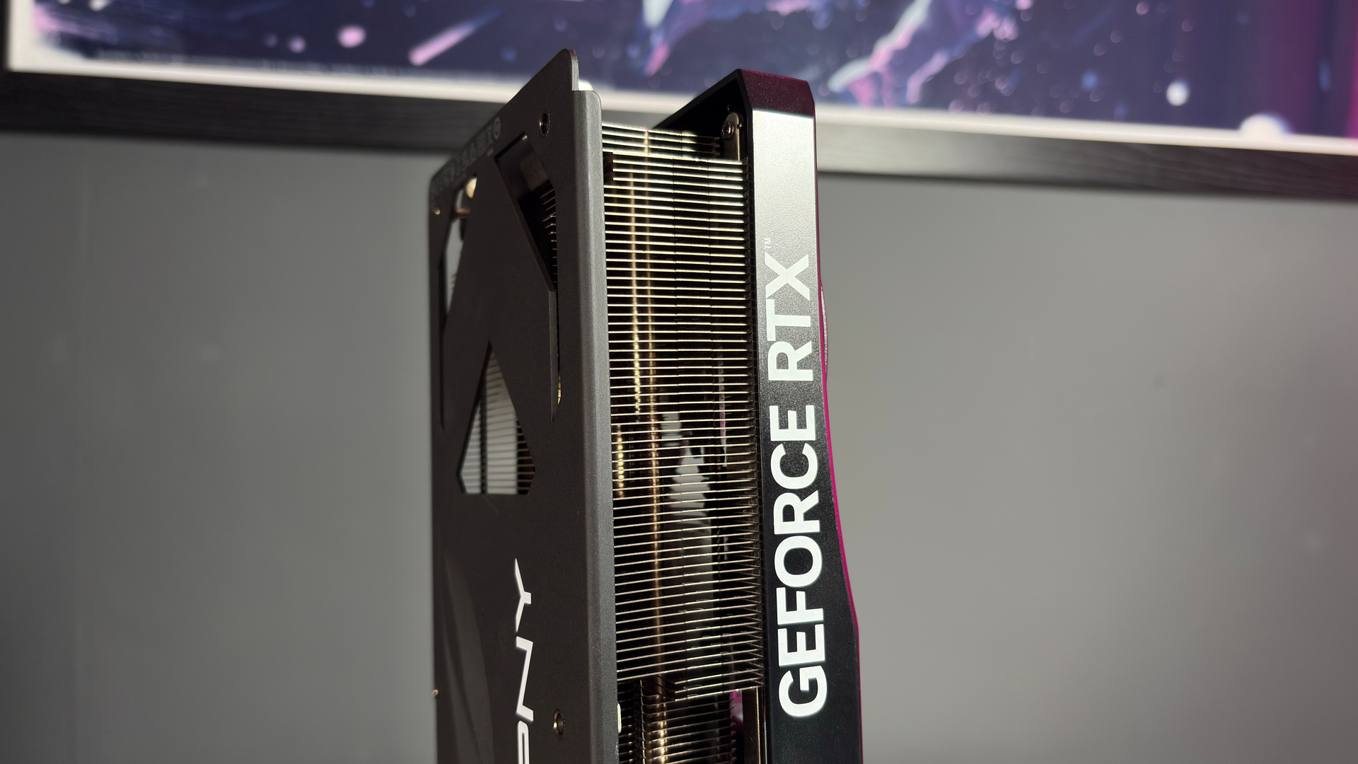 A PNY RTX 5070 Ti OC graphics card on a desk with a desk mat and pink light.