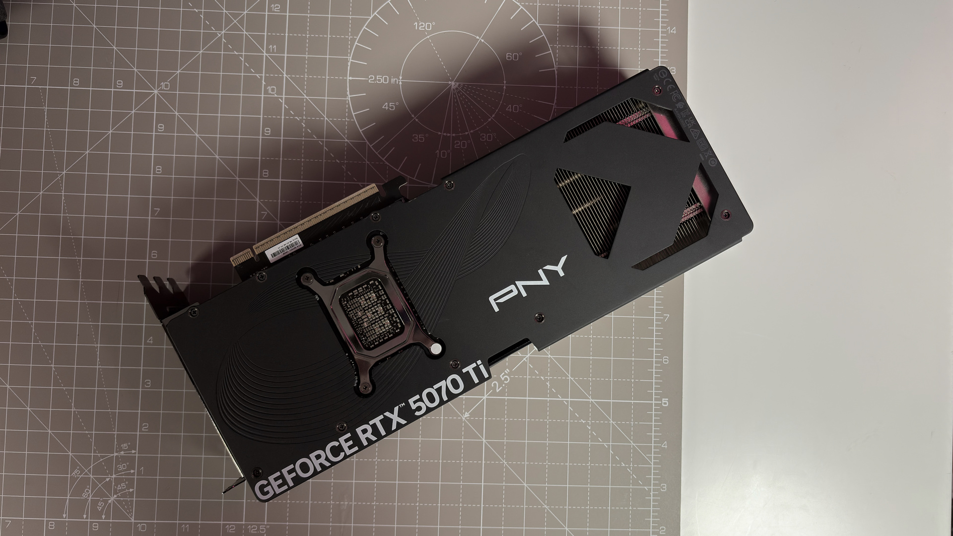 A PNY RTX 5070 Ti OC graphics card on a desk with a desk mat and pink light.